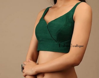 Pode incluir: Um top curto sem mangas de cor verde escuro com um decote em V profundo e uma única costura no centro. O top é feito de um tecido macio e sedoso e tem um caimento solto. O texto "Balaji Boutique" é visível no canto inferior direito do top.