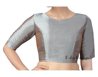Puede incluir: Una blusa plateada sin mangas con cuello redondo y mangas cortas. La blusa está hecha de una tela brillante y tiene una silueta ajustada. El texto "Balaji Boutique" está impreso en el lado derecho de la blusa.
