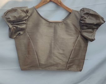 Puede incluir: Una blusa marrón sin mangas con mangas abullonadas. La blusa tiene un escote redondo y está hecha de una tela sedosa. El texto "Balaji Boutique" está impreso en la esquina inferior derecha de la blusa.