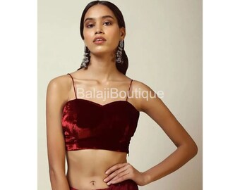 May include: A maroon velvet crop top with a sweetheart neckline and thin straps. The top is being modelled by a woman with long dark hair and silver earrings.