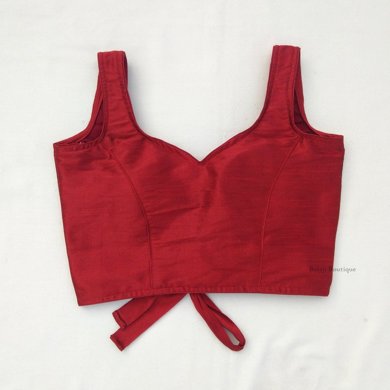 May include: A maroon sleeveless blouse with a sweetheart neckline and a tie at the back. The blouse is made of a smooth, silky fabric.