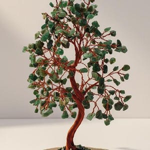 May include: A decorative tree sculpture with a copper wire trunk and branches, adorned with green gemstone leaves. The tree sits on a natural agate slice base, creating a unique and artistic display. The sculpture is approximately 8 inches tall.