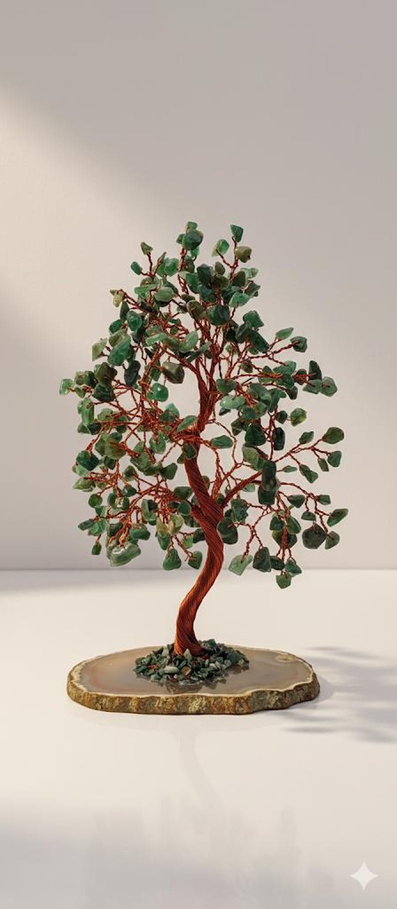May include: A decorative tree sculpture with a copper wire trunk and branches, adorned with green gemstone leaves. The tree sits on a natural agate slice base, creating a unique and artistic display. The sculpture is approximately 8 inches tall.