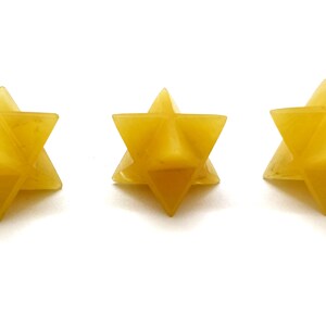 May include: Three yellow star-shaped objects are arranged in a row against a white background. Each star has six points and a geometric design. The objects appear to be made of a translucent material.