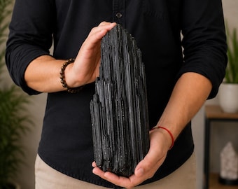 May include: A large, raw black tourmaline crystal specimen featuring a tall, elongated shape with prominent vertical striations and a jagged, crystalline texture. The stone is opaque, deep black in color, and displays a natural, unpolished surface.