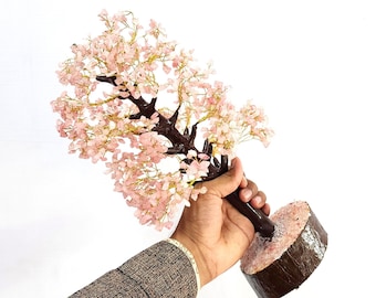 Pode incluir: Uma árvore de cristal rosa com uma base de madeira marrom. A árvore é feita de pequenos cristais rosa que são unidos por fios para formar galhos. A base é uma peça de madeira grossa e redonda com uma textura áspera.