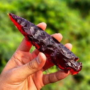 May include: A red obsidian arrowhead with a sharp point and a textured surface.