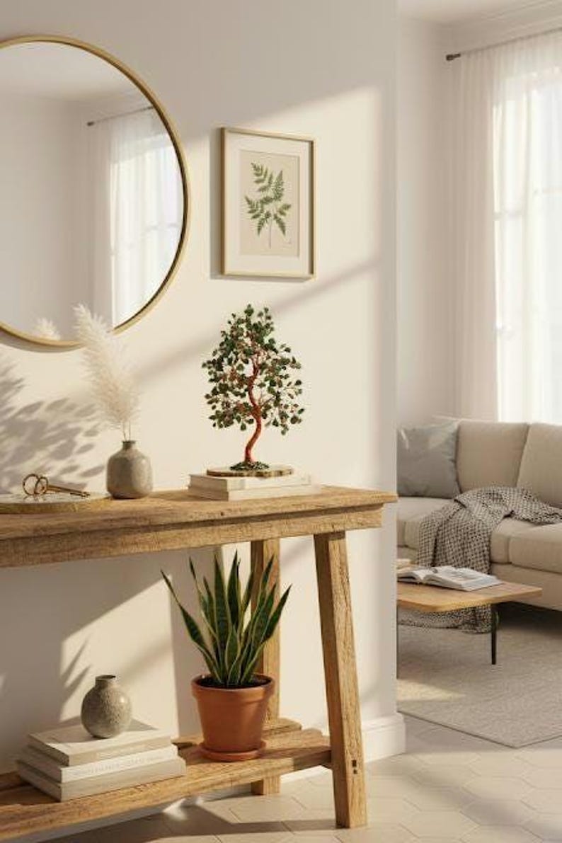 May include: A wooden console table with a decorative tree sculpture, a framed botanical print, and a potted snake plant. A round gold mirror hangs on the wall above the table. The room has a neutral color palette.