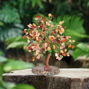 May include: A gemstone tree sculpture with a copper wire trunk and branches, decorated with colourful gemstone chips. The tree sits on a round, speckled stone base, creating a natural and artistic display. Gemstones include pink, green, orange, and purple.