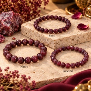 Pode incluir: Três pulseiras de contas vermelho-escuras são exibidas. Uma pulseira apresenta contas redondas lisas de 8 mm, outra tem contas redondas lisas de 10 mm e a terceira consiste em contas facetadas. Cada pulseira está rotulada com seu tamanho.