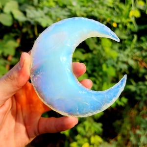 May include: A crescent moon shaped piece of iridescent opal, with a light blue and white colour.