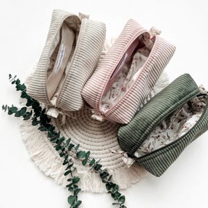 Könnte beinhalten: Drei rechteckige Reißverschlusstaschen aus geripptem Cordstoff in Creme, Altrosa und Olivgrün. Jede Tasche verfügt über ein blumenbedrucktes Innenfutter und ein kleines weißes Stoffetikett mit dem Text maimozelle im Inneren.