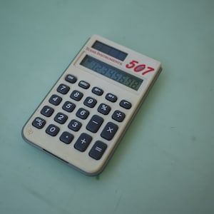 May include: A vintage Texas Instruments 507 calculator with a cream-colored body and black buttons. The display shows the number 12345678. The calculator has a red "507" logo and the brand name "TEXAS INSTRUMENTS" printed on the top.