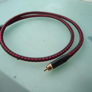 May include: A red and black audio cable with gold-plated connectors. The cable has a braided design with a repeating pattern of red and black. The connectors are black with gold tips.