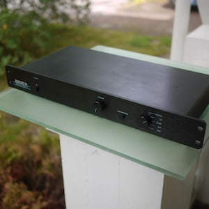 Op de afbeelding: Een zwarte audio-voorversterker met een rechthoekige metalen behuizing. Het voorpaneel is voorzien van twee ronde bedieningsknoppen, een kleine aan-uitknop en tekstlabels waaronder 8800-X, Volume, Input Selector, Phono, CD, Tuner, Aux en Tape.