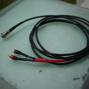 May include: Black audio cable with a silver connector and RCA connectors. The cable is coiled and has a red section near the RCA connectors. The connectors are gold-colored.
