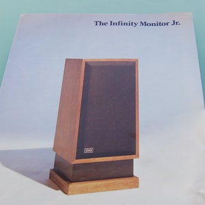 May include: A vintage speaker cabinet with a wooden frame and a dark brown speaker cover. The text "The Infinity Monitor Jr." is printed at the top. The speaker has a rectangular shape and is set on a wooden base.