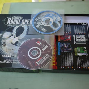 Puede incluir: Un juego de caja de video Rainbow Six Rogue Spear Platinum Jacket. La caja negra presenta gr&aacute;ficos en blanco y gris, e incluye dos CD en fundas de pl&aacute;stico. El t&iacute;tulo y el logotipo del juego se muestran de forma destacada en la caja.
