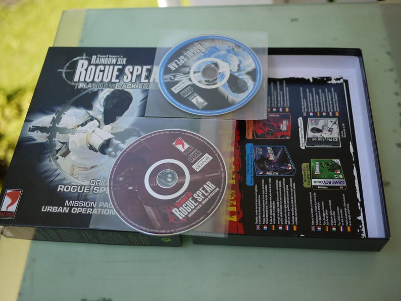 Puede incluir: Un juego de caja de video Rainbow Six Rogue Spear Platinum Jacket. La caja negra presenta gr&aacute;ficos en blanco y gris, e incluye dos CD en fundas de pl&aacute;stico. El t&iacute;tulo y el logotipo del juego se muestran de forma destacada en la caja.
