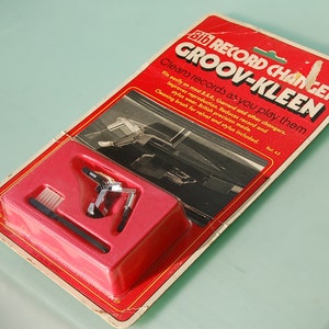 Può includere: Un kit di pulizia per giradischi Groov-Kleen vintage nella sua confezione originale. La confezione rossa e bianca contiene un pulitore per dischi, una spazzola per la pulizia e altri accessori. Il testo sulla confezione recita "Pulisce i dischi mentre li suoni."