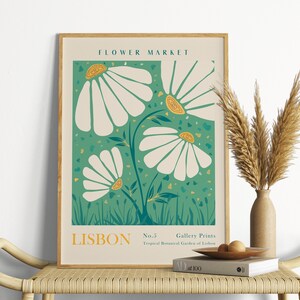 May include: A framed poster with a green background and white flowers with yellow centers. The poster says "FLOWER MARKET" at the top and "LISBON No.5 Gallery Prints Tropical Botanical Garden of Lisbon" at the bottom.