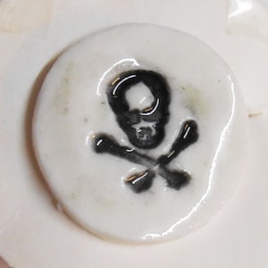 May include: A white ceramic plate with a black and white skull and crossbones design.
