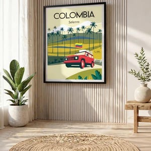 May include: Framed poster featuring a stylized illustration of Colombia's Solento region. The artwork depicts a red vehicle on a road, palm trees, and the Colombian flag. The poster is displayed in a room with a neutral color palette.