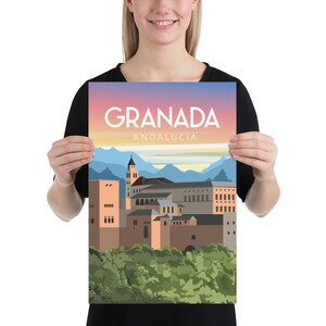 May include: A poster featuring a stylized illustration of Granada, Andalusia, with the city's name in large white letters. The artwork depicts buildings, mountains, and a colorful sunset sky. The poster is held by a person.