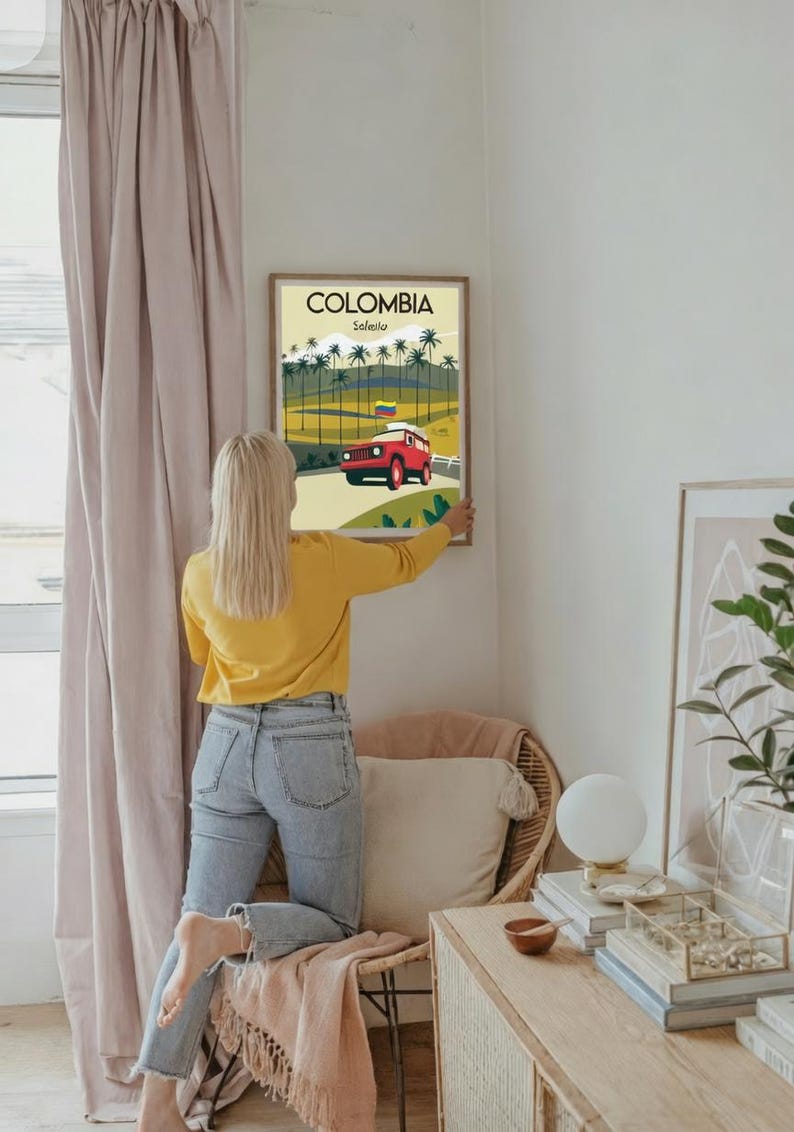 May include: A framed poster with the word "COLOMBIA" at the top, and "Salento" below it. The poster features a red jeep driving on a road, with palm trees and a Colombian flag. The poster is being hung on a white wall.