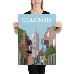 May include: A colorful illustration of a street scene in Cartagena, Colombia. The image features a narrow street lined with colorful buildings, lush greenery, and a tall church tower in the background. The text "COLOMBIA CARTAGENA" is displayed at the top of the image.