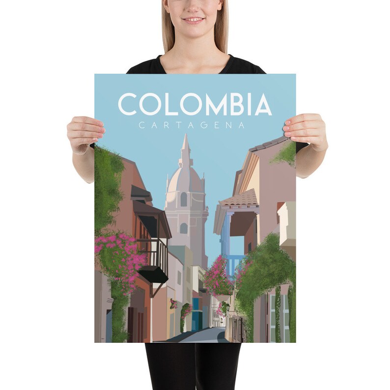 May include: A colorful illustration of a street scene in Cartagena, Colombia. The image features a narrow street lined with colorful buildings, lush greenery, and a tall church tower in the background. The text "COLOMBIA CARTAGENA" is displayed at the top of the image.
