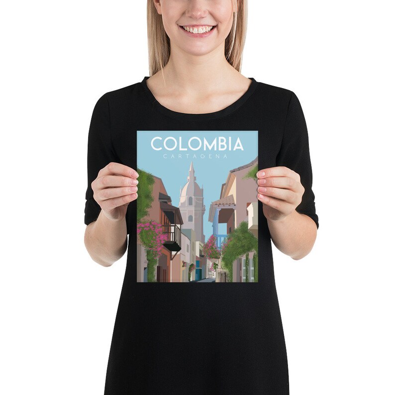 May include: A colorful illustration of a street scene in Cartagena, Colombia. The illustration features a narrow street lined with colorful buildings, a tall church tower, and lush greenery. The text "COLOMBIA CARTAGENA" is displayed at the top of the illustration.