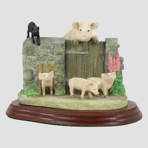 May include: A decorative figurine featuring a stone wall with a wooden gate, and several pig figurines. A black cat figurine is perched on the wall. The base is a dark brown, round shape. The pigs are light beige and the gate is green.