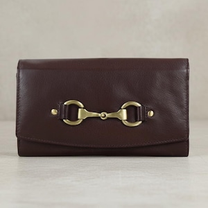 May include: A dark brown leather wallet with a gold-coloured metal clasp. The wallet is rectangular with a flap closure. The clasp is a decorative element, adding a touch of elegance to the accessory.