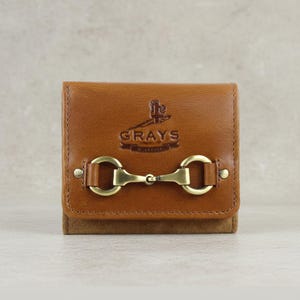 May include: A tan leather wallet featuring a brass-coloured horse bit clasp. The wallet is embossed with the word "GRAYS". The lower section of the wallet is made of a darker brown suede material.
