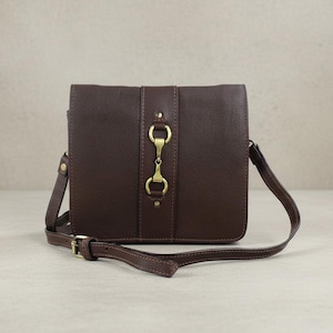 May include: A brown leather crossbody bag with a rectangular shape. The bag features a long, adjustable strap and a decorative gold-coloured clasp. The bag has a textured surface and is designed with a flap closure.