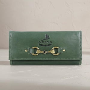 May include: A green leather wallet with a brass-coloured clasp. The wallet features a flap closure and the "GRAYS" logo in black. The design is simple and elegant, suitable for everyday use.