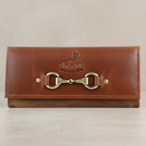 May include: A brown leather wallet with a brass-coloured clasp. The wallet features a suede base and a flap closure. The brand name "GRAYS" is embossed on the front. A stylish accessory for everyday use.