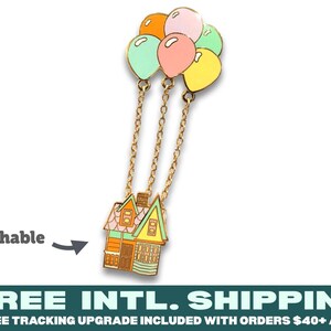 May include: A metal enamel pin featuring a house with a light green roof and orange walls, suspended by three gold-toned chains from a cluster of five pastel-colored balloons in orange, pink, yellow, and light green. The word Detachable is printed nearby.