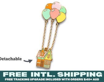 May include: A metal enamel pin featuring a house with a light green roof and orange walls, suspended by three gold-toned chains from a cluster of five pastel-colored balloons in orange, pink, yellow, and light green. The word Detachable is printed nearby.