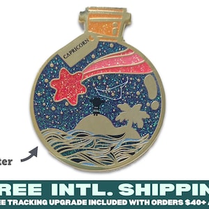 Pode incluir: Pin de esmalte dourado em forma de garrafa com um design de glitter azul, verde e rosa. A garrafa contém uma estrela, uma palmeira e uma pequena figura em pé numa ilha. O texto "CAPRICORN" está na garrafa.