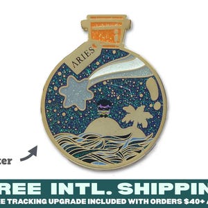 May include: A round gold-toned enamel pin shaped like a bottle with an orange stopper. The interior features a dark blue glitter night sky with a shooting star, a small island with a palm tree, and stylized ocean waves. A tag reads ARIES.