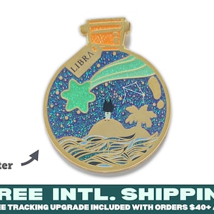 Pode incluir: Pin de esmalte dourado com a forma de uma garrafa redonda de vidro com rolha de cortiça. A garrafa contém um céu noturno cheio de glitter azul e verde com uma estrela cadente, uma pequena ilha, uma palmeira e a constelação de Libra. O rótulo na garrafa diz "LIBRA".