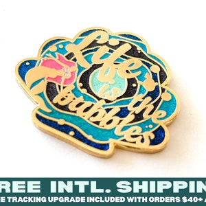 Puede incluir: Pin esmaltado dorado con la frase "Life is the bubbles". El diseño azul y turquesa incluye una flor rosa y burbujas. Un accesorio decorativo y divertido.