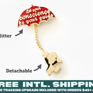 Könnte beinhalten: Goldfarbener Pin mit einem roten Glitzer-Regenschirm mit dem Text "Let your conscience be your guide" und einer goldfarbenen Figur, die den Regenschirm hält. Der Regenschirm und die Figur sind abnehmbar.