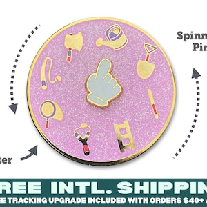 May include: A pink glitter enamel pin with a spinning pin in the center. The pin features a variety of gardening tools, including a watering can, shovel, rake, magnifying glass, slingshot, axe, and ladder. The pin is surrounded by a gold border.