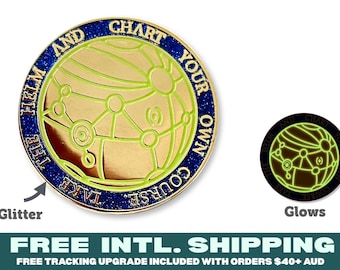 May include: A round gold-toned metal pin featuring a globe design with light green lines and a dark blue glitter border. The text "TAKE THE HELM AND CHART YOUR OWN COURSE" is embossed along the edge. A smaller version of the pin is shown glowing in the dark.