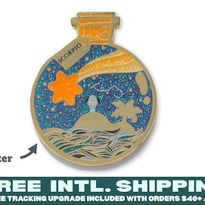 May include: A gold-toned metal enamel pin shaped like a bottle containing a night sky scene with a glittery blue background, a bright orange star, a palm tree on a small island, and the word SCORPIO printed on a small tag attached to the neck.