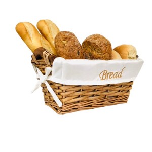 May include: A wicker basket containing a selection of breads. The basket holds baguettes, round loaves, and a roll. A white cloth inside the basket has the word "Bread" embroidered on it.