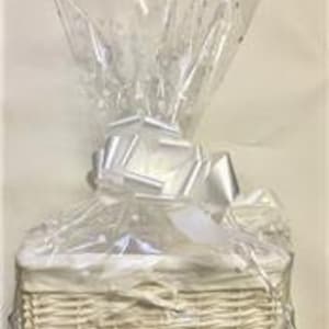 May include: White wicker basket with a white satin ribbon and clear cellophane wrapping. The basket is filled with various items, including a white candle and a bottle of wine.